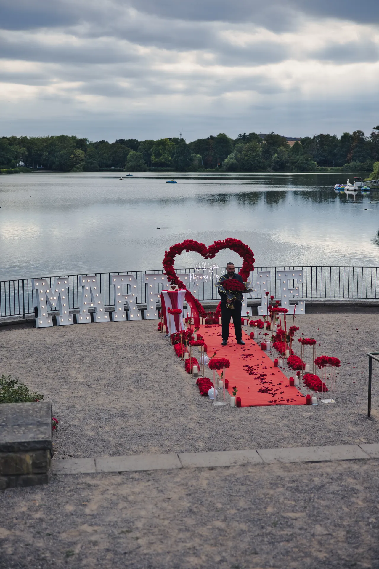 Antragsteller wartet mit Rosenstrauß vor der Heiratsantrag-Dekoration am Berger See